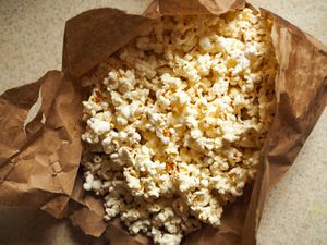 A torn open brown paper lunch bag holding popped popcorn.