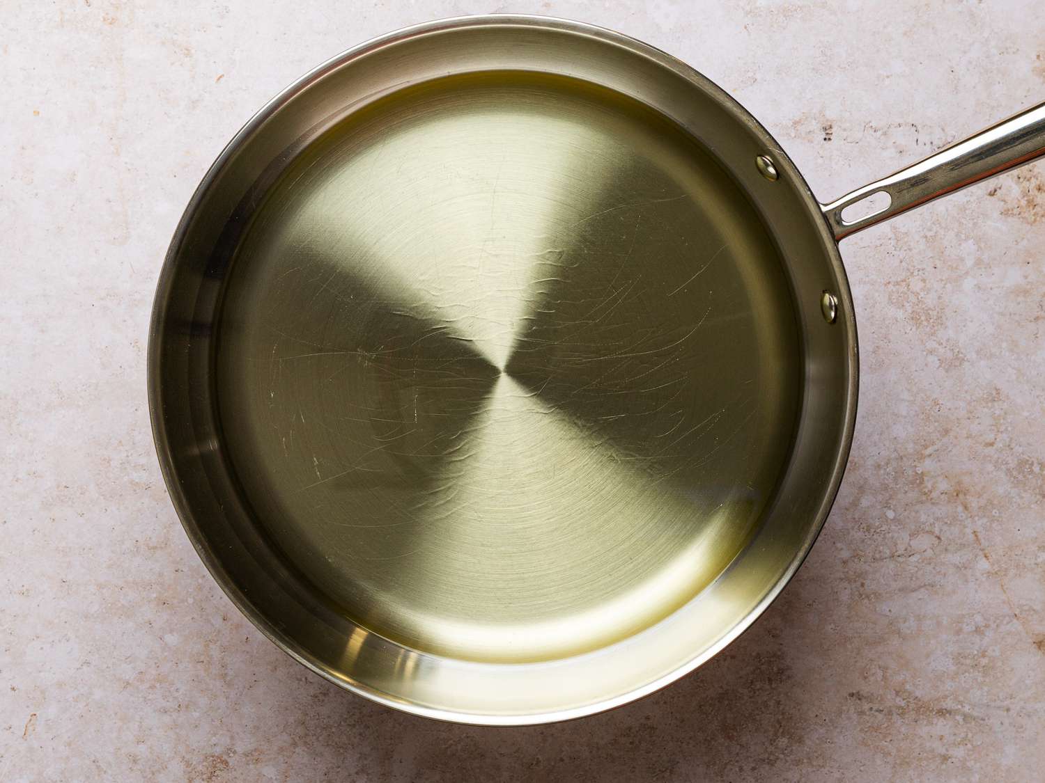 Hot, shimmering oil inside of a stainless steel saute pan.