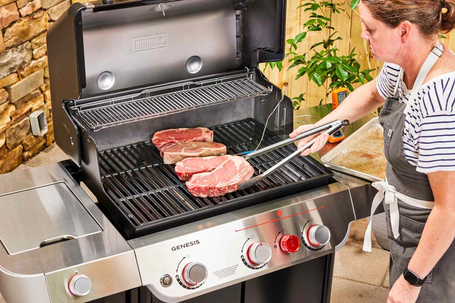 A person cooks steaks in the Weber Genesis E-335 Gas Grill