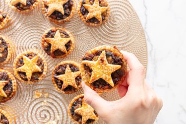 Decorative platter of baked minced pies, with hand holding one pie close up 