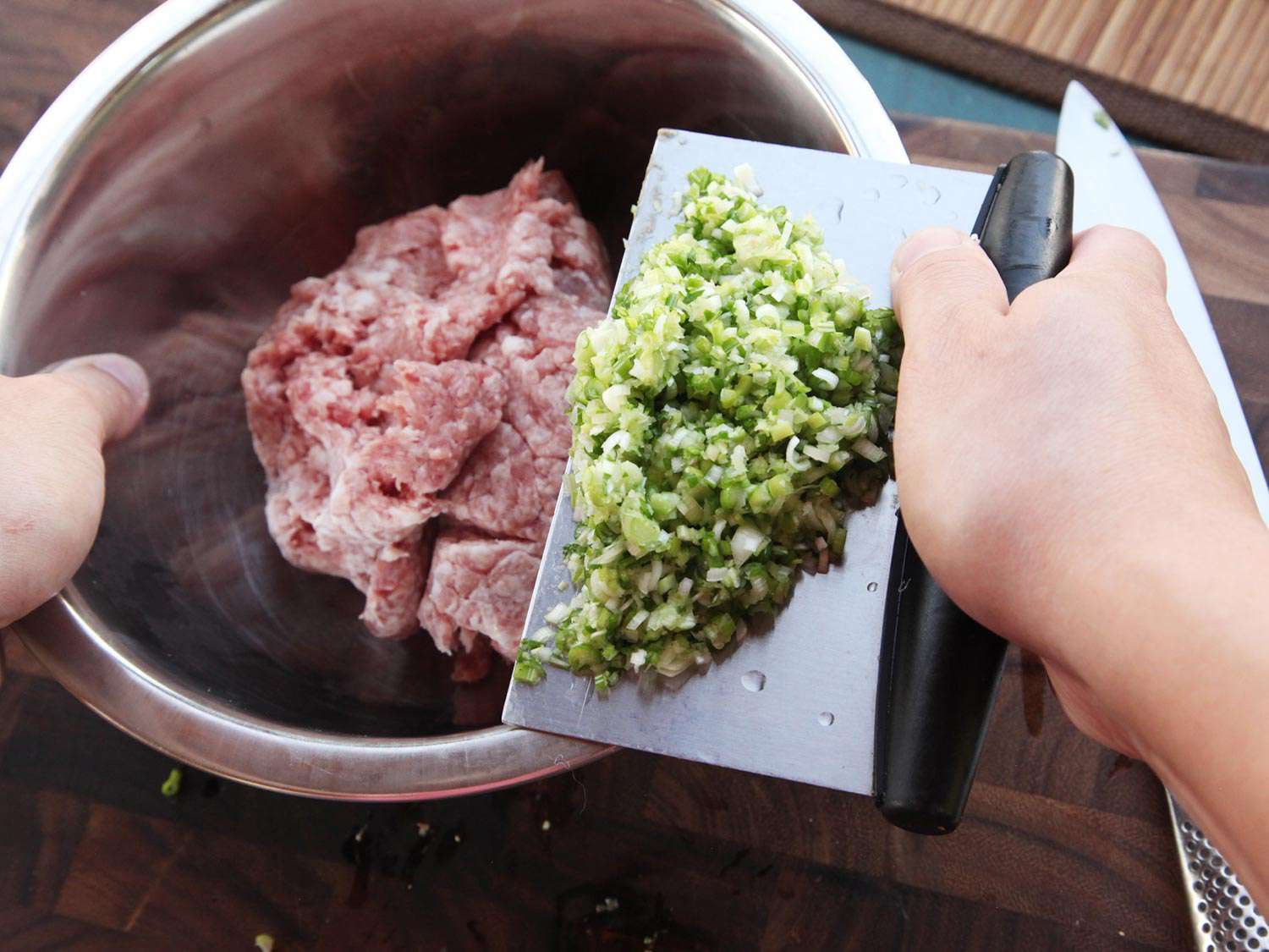 Adding finely minced garlic, ginger, and scallions to a bowl with raw pork. 