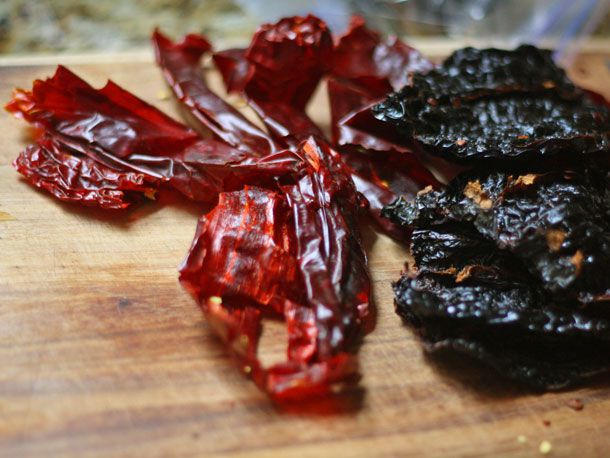 A variety of dried red chiles stemmed and seeded on a wooden cutting board.
