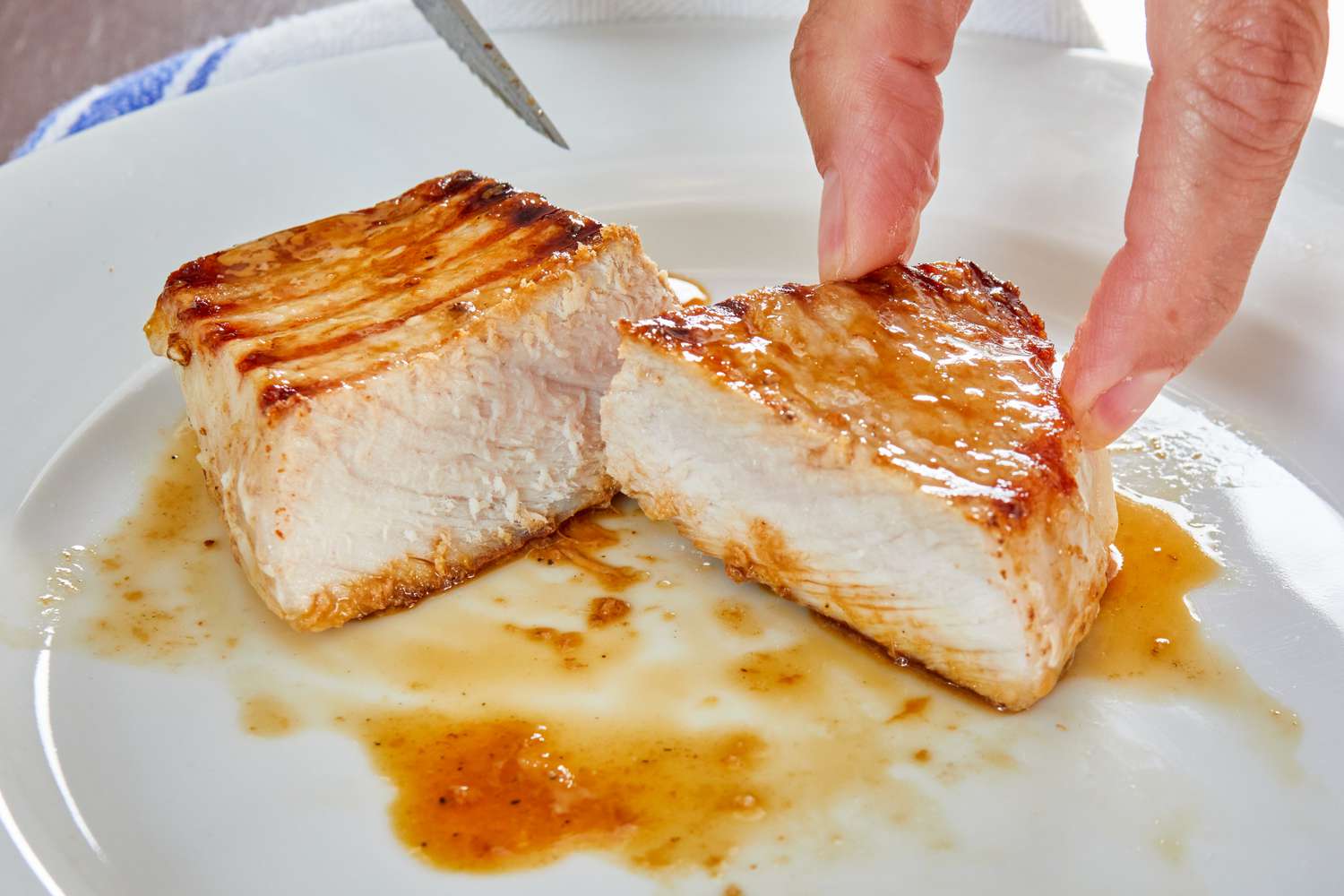 A person cutting a grilled pork chop in half on a plate 