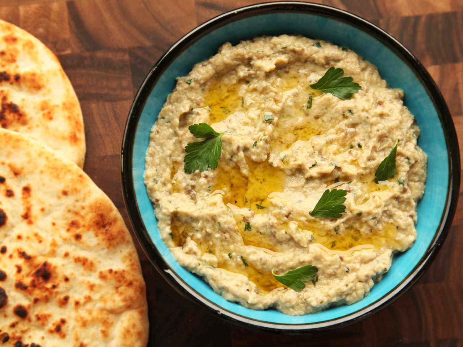 Overhead of a stoneware bowl of baba ganoush, next to charred and blistered flatbreads