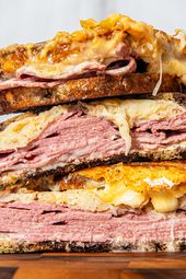 Three reuben sandwich halves stacked on top of each other on a cutting board
