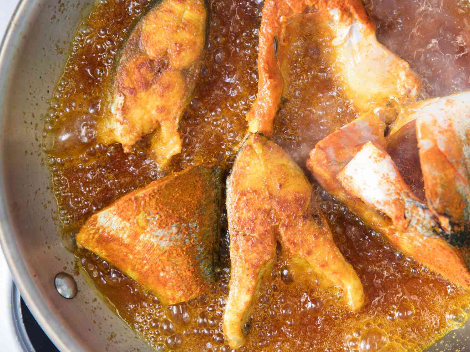A stainless steel pan holding the seasoned fish steaks being fried in oil.