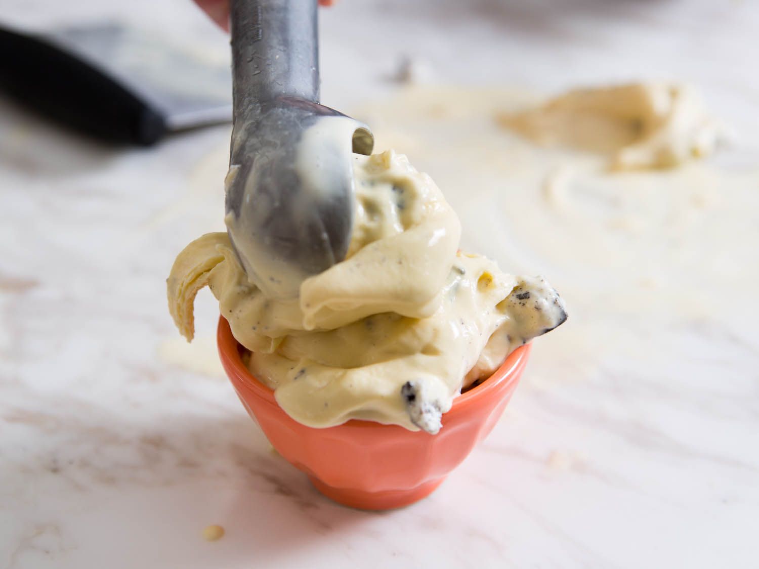 Scooping chewy New England-style ice cream that has been stretched on a marble surface into a serving bowl. 