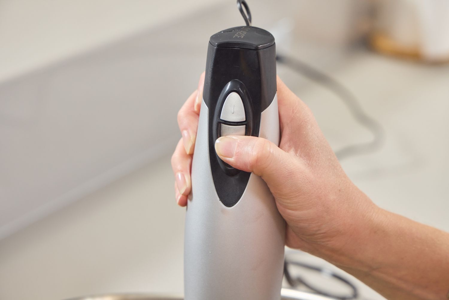 A person presses a button on the Hamilton Beach 2-Speed Hand Blender