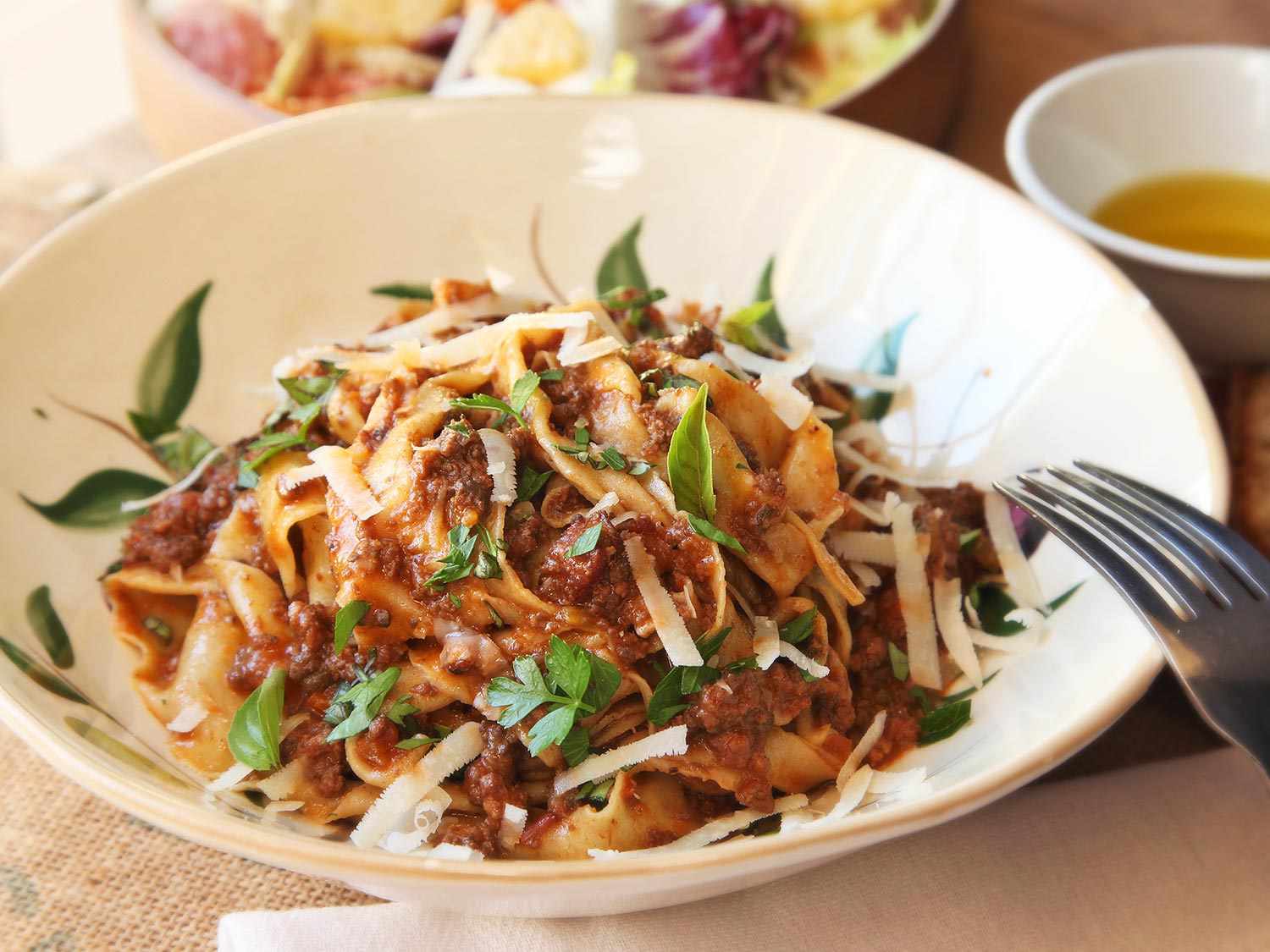 A serving of the sauced pasta in a shallow bowl, garnished with parsley, basil, and wide Parmesan shavings.
