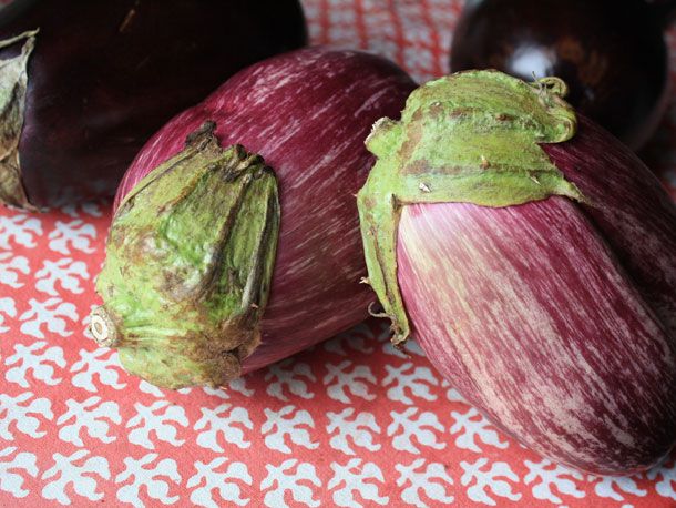 Several eggplants lay on a tablecloth. A few have light purple, variegated skin.