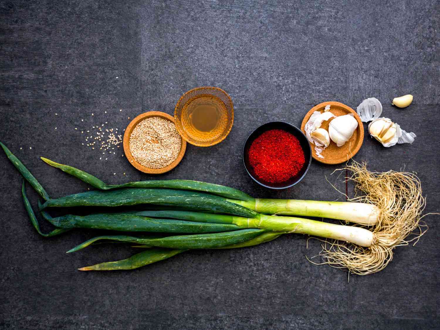 An assortment of seasonings: roasted sesame seeds, sesame oil, gochugaru, garlic, and daepa (or Welsh onion).