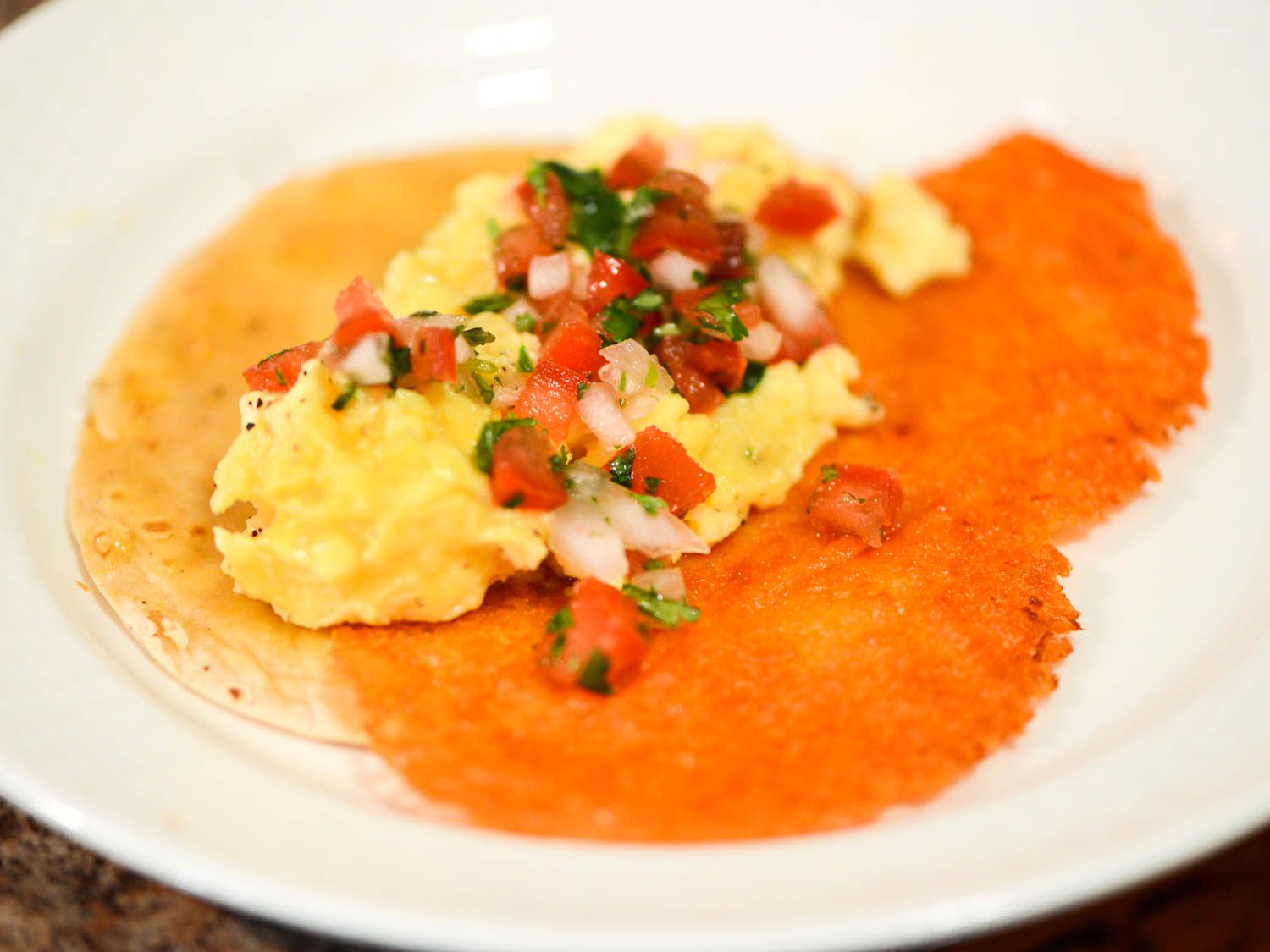 A crispy cheese taco, topped with scrambled eggs and pico de gallo. 