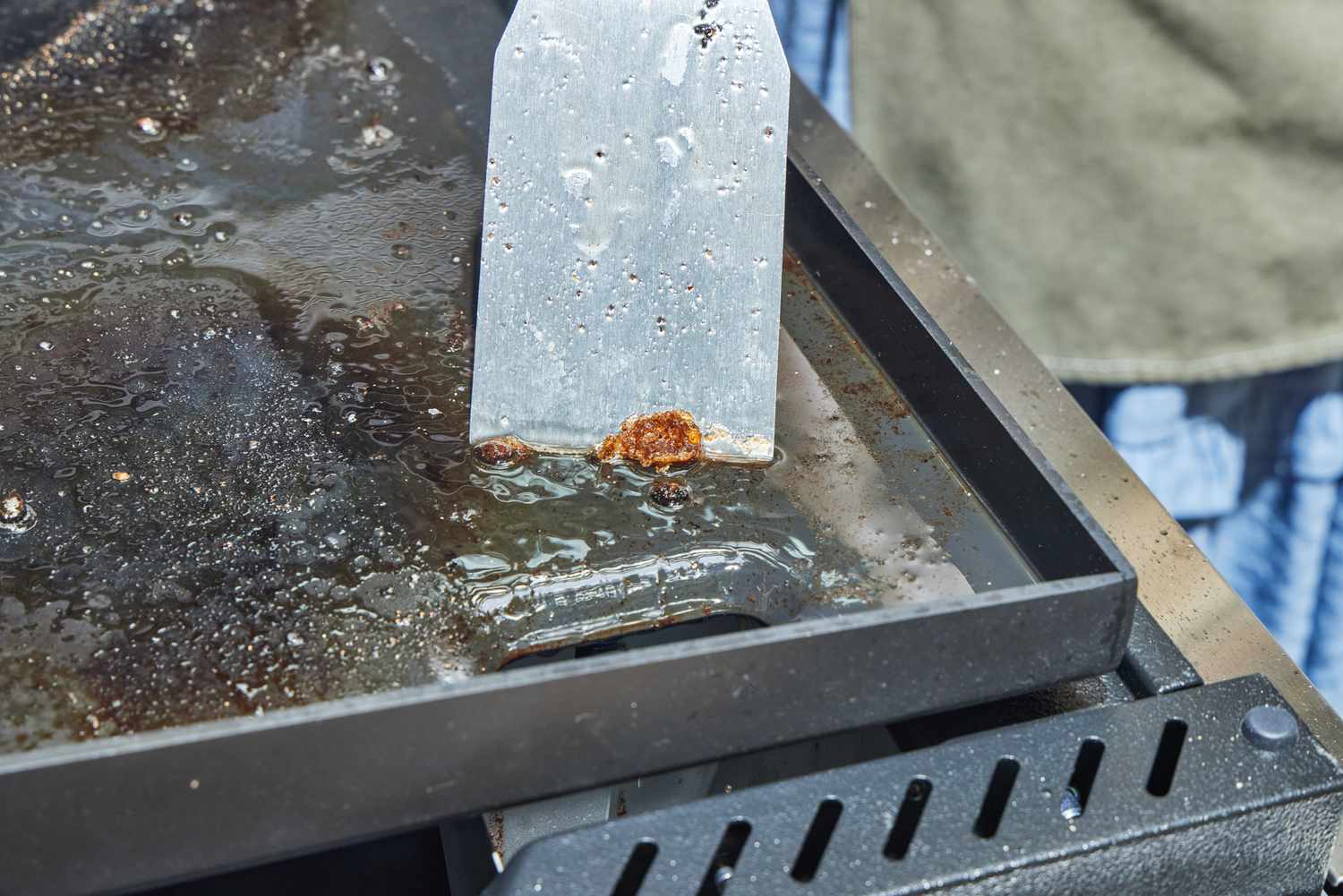 A person cleans the top of the Weber Slate 30 Inch Griddle with a spatula