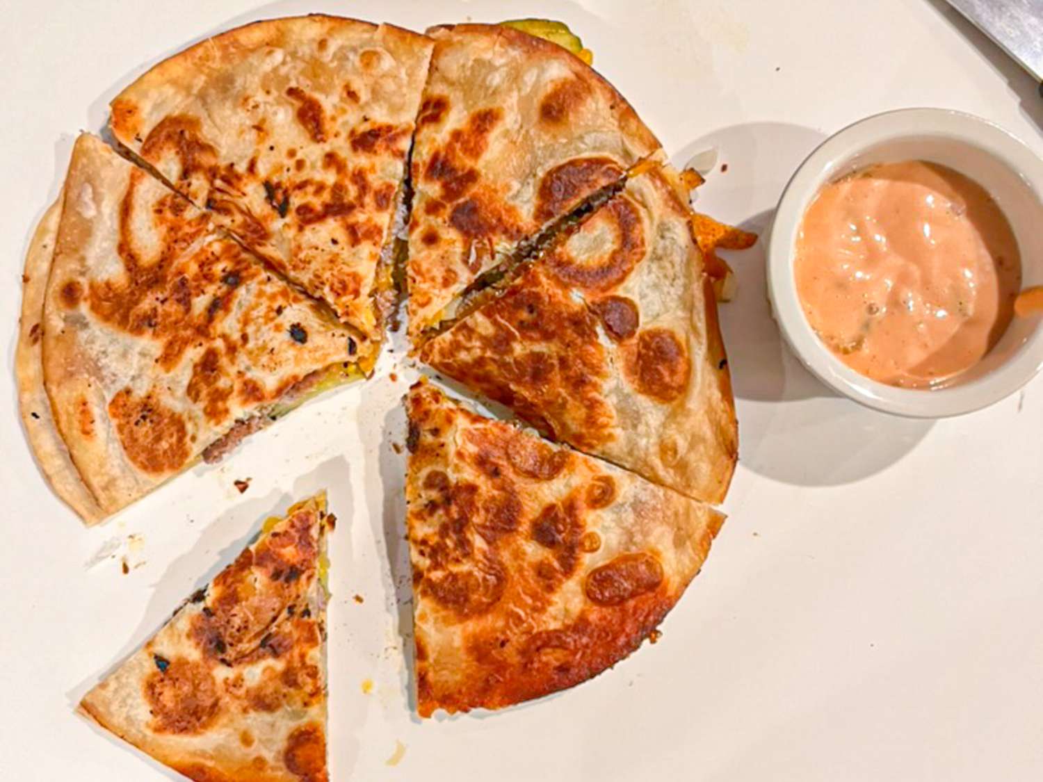 A smashed burger quesadilla sliced into six pieces with special sauce on the side