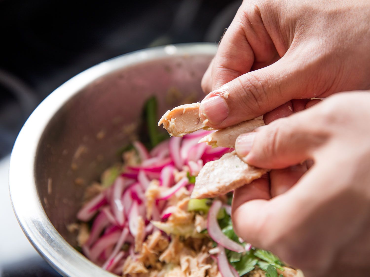 Author breaks apart drained ventresca tuna into large flakes by hand over a mixing bowl.