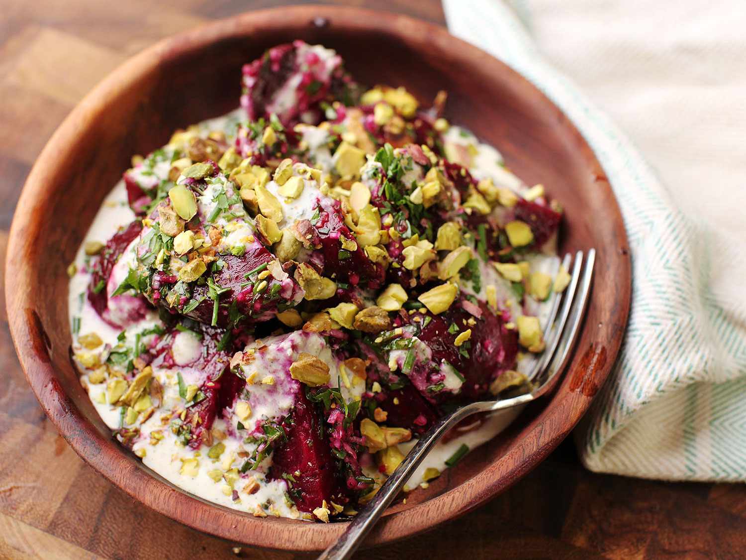 Roasted beets with creamy horseradish sauce and pistachios served up in a wooden bowl with a fork