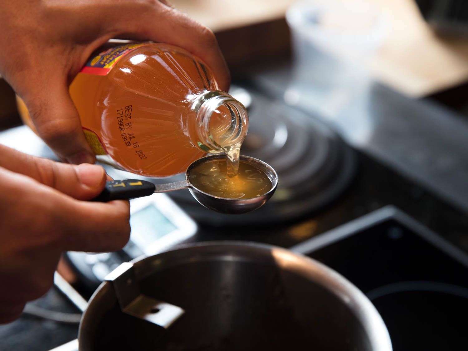 Measuring a tablespoon of apple cider vinegar over a saucepan to make candied yams (sweet potatoes).