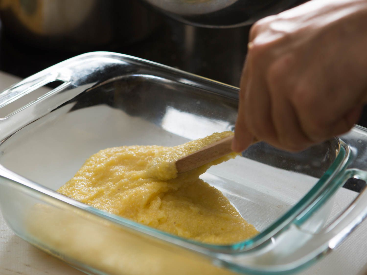 Cooked polenta is spooned into a baking dish and spread into a thin layer.