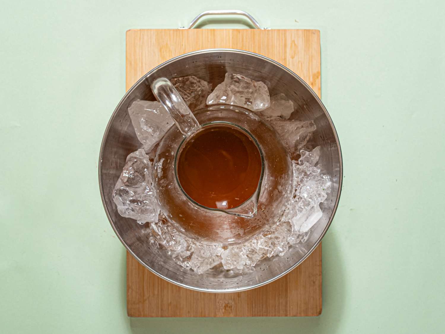 A container with a pitcher of liquid surrounded by ice on a cutting board