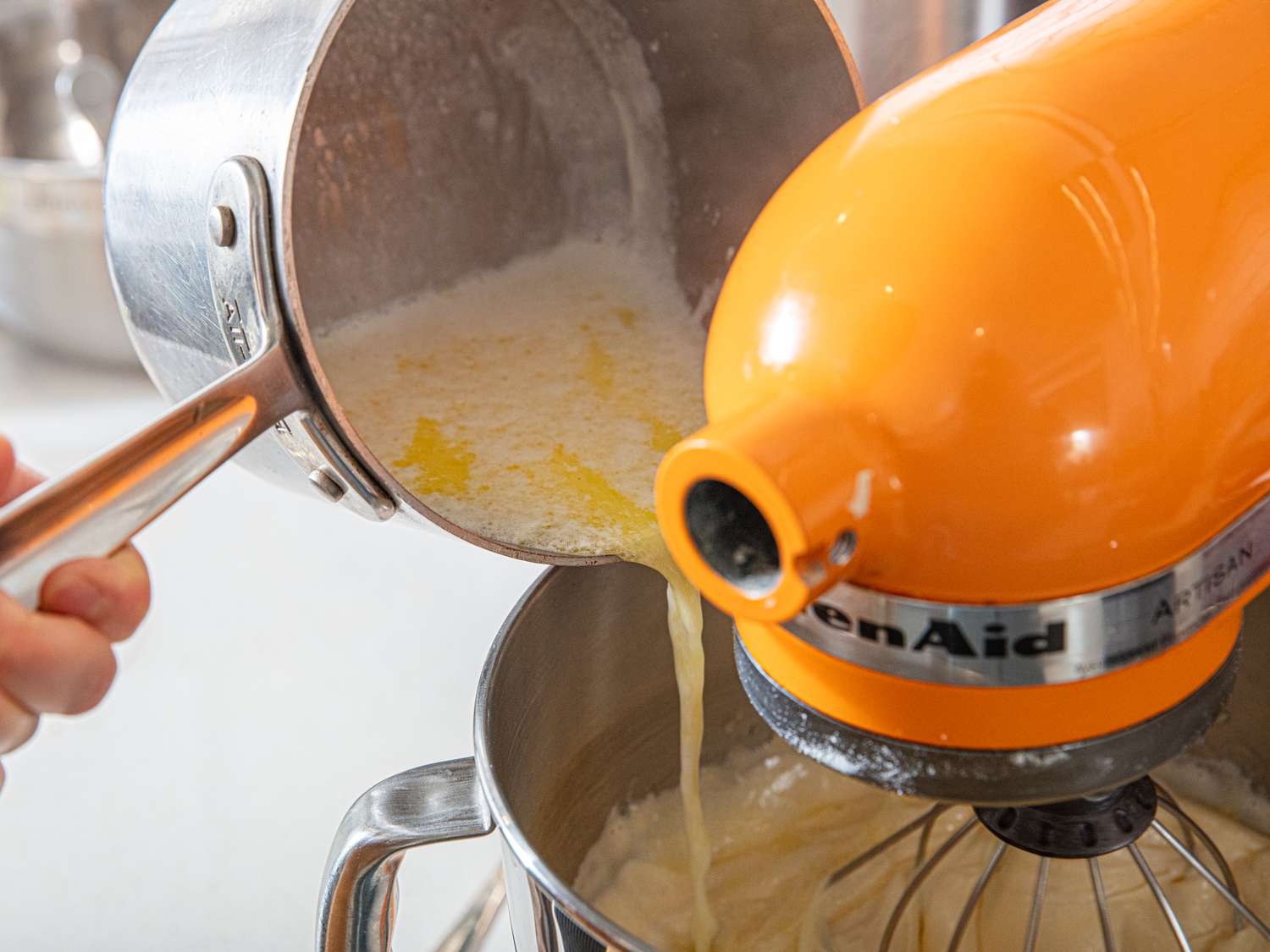 Pouring a mixture into a stand mixer bowl during baking preparations