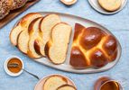 Entire loaf of plain woven challah on a plate, surrounded by smaller plates, salt, honey and a cup of tea