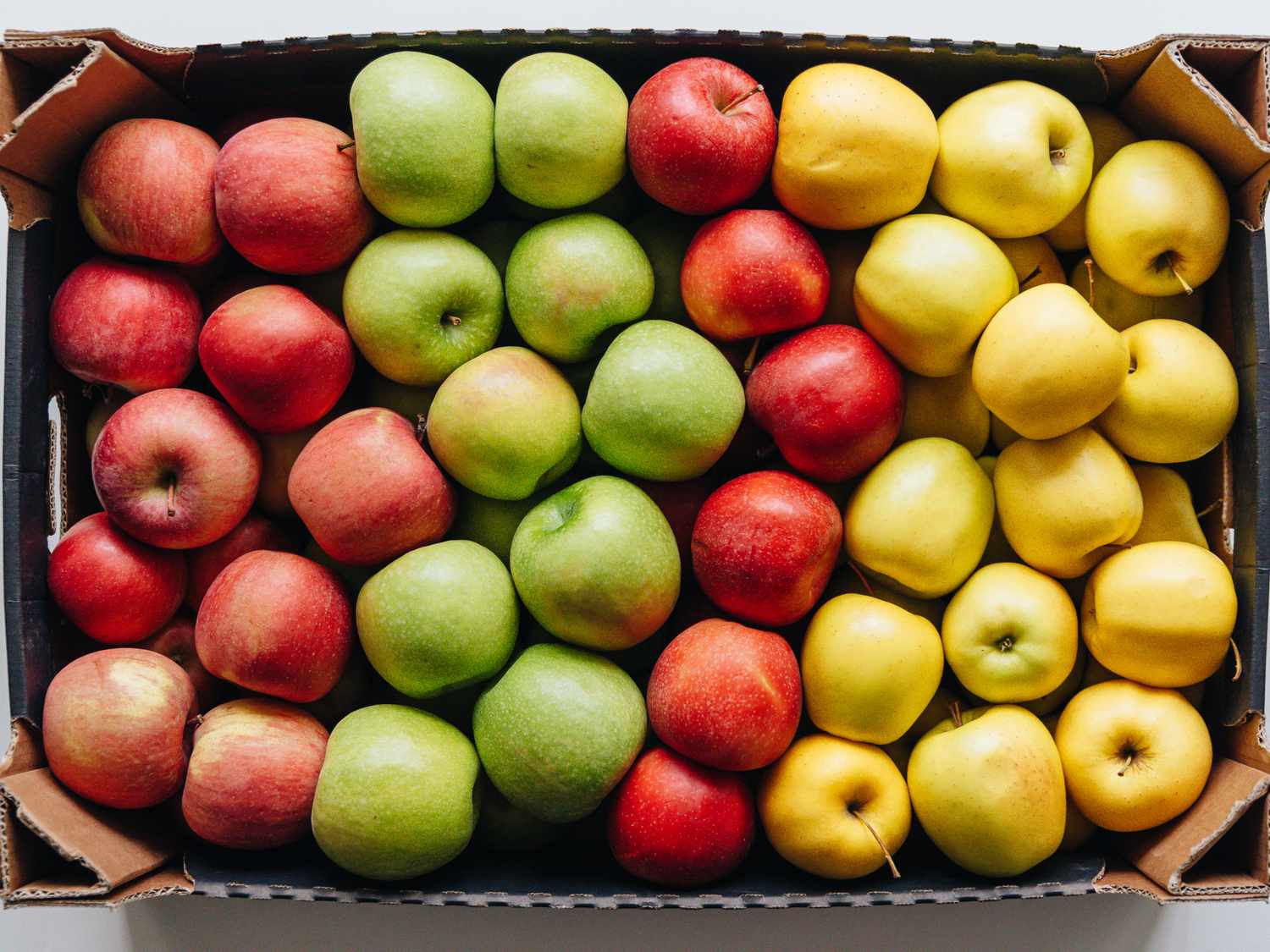 Assorted apples organized in rows within a cardboard tray