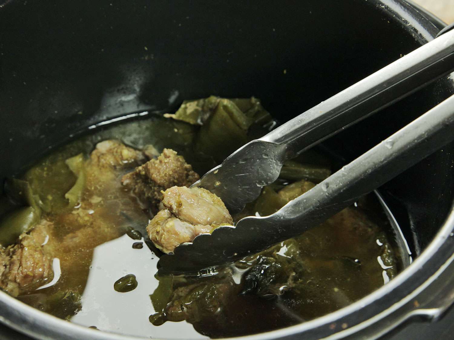 Tongs removing the pork from a pressure cooker chile verde stew.