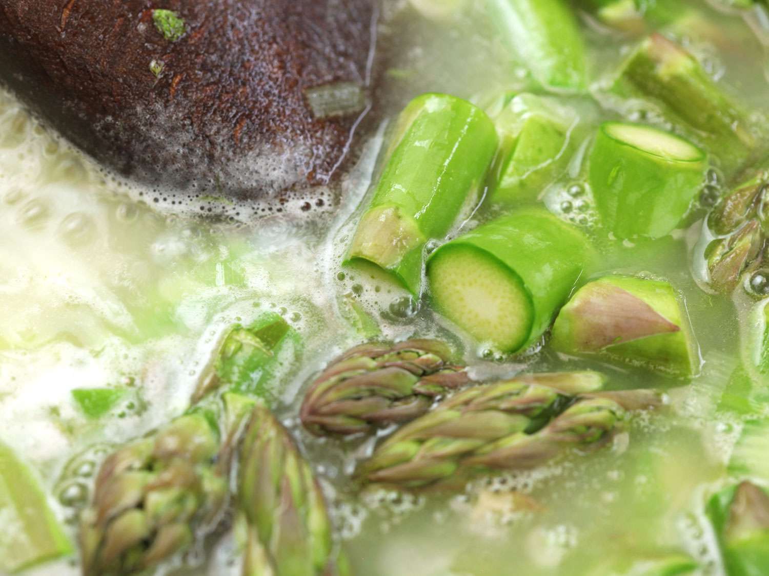 Closeup of asparagus pieces simmering in stock.