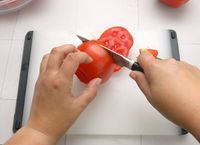 a person slicing a tomato with a paring knife