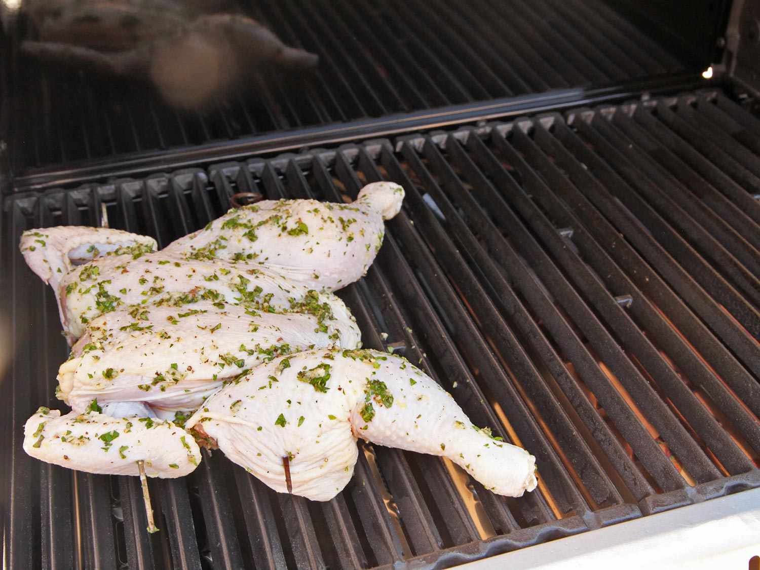 A butterflied chicken being grilled on a charcoal grill. 