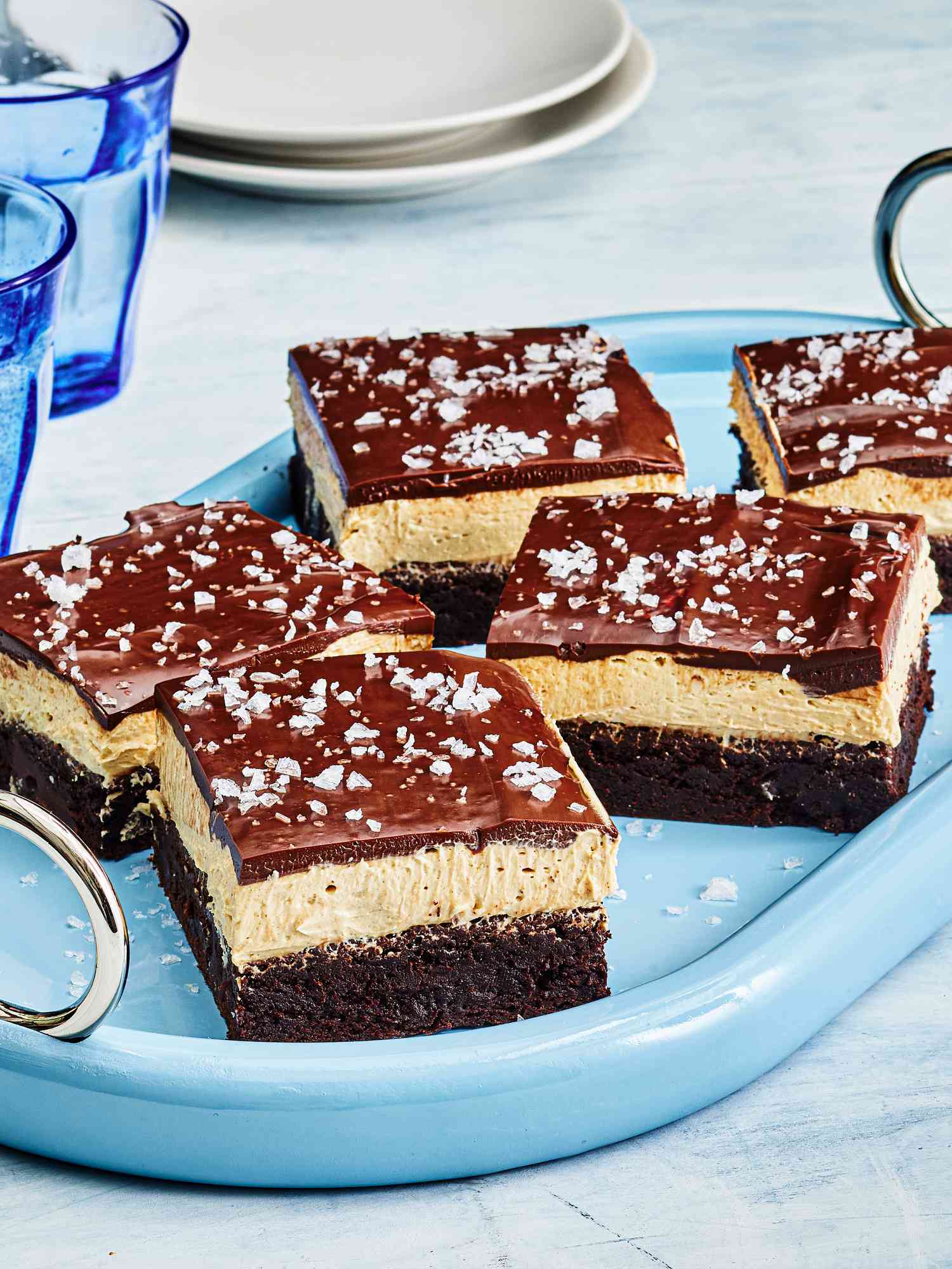Buckeye Brownies with sea salt garnish, cut into pieces on a blue dish, with blue cups and small white plates 