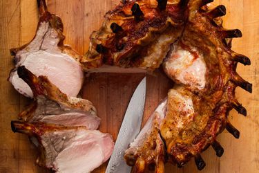 A crown roast of pork on a cutting board, three chops have been cut from the roast. 