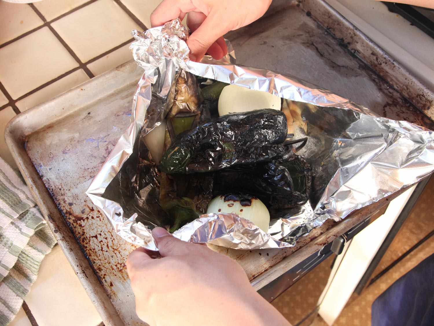 Hands pulling foil around charred peppers, onion, and garlic.