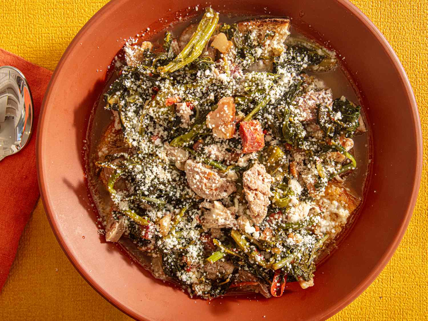 A bowl of Italian wedding soup with greens meat and grated cheese