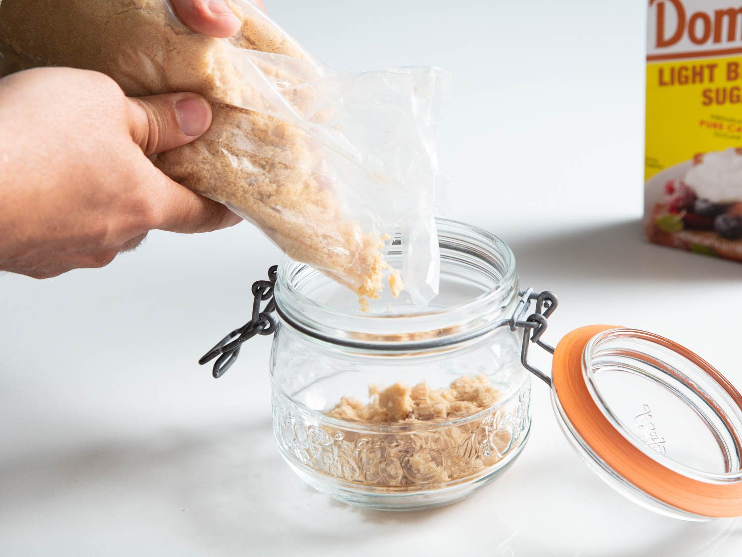 Pouring brown sugar from its bag into an airtight glass container with a rubber gasket lid.