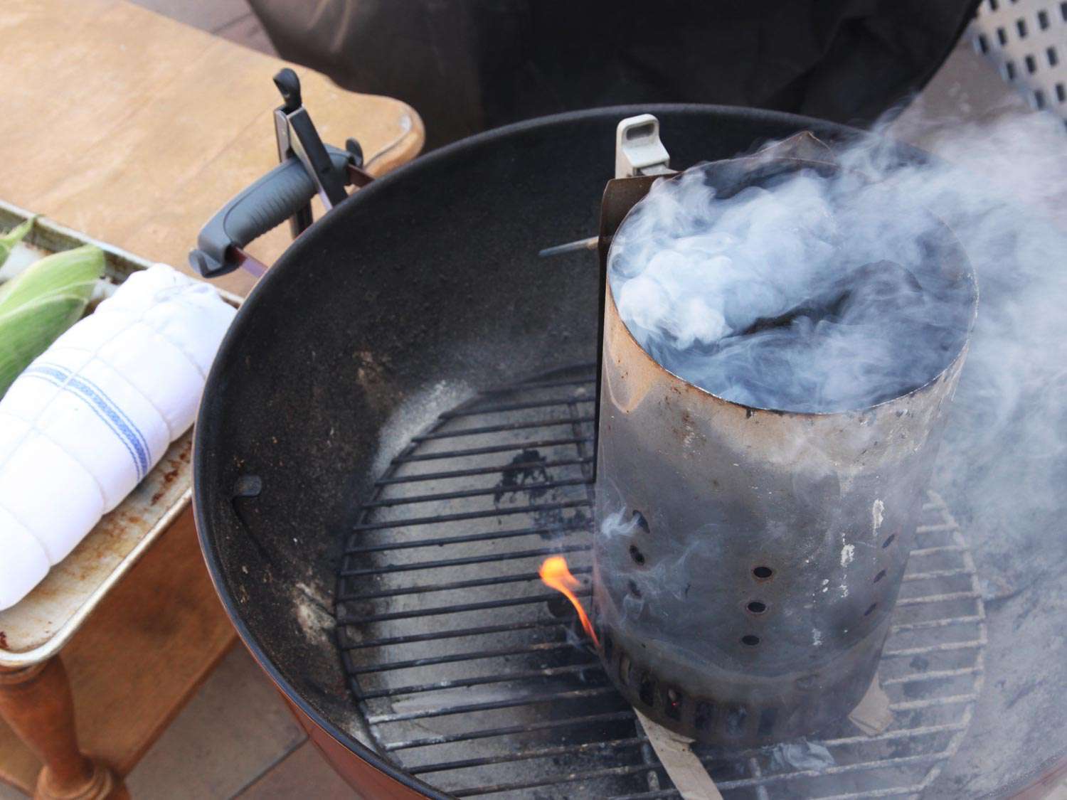 A chimney of charcoal catches and smokes in a kettle-style grill.