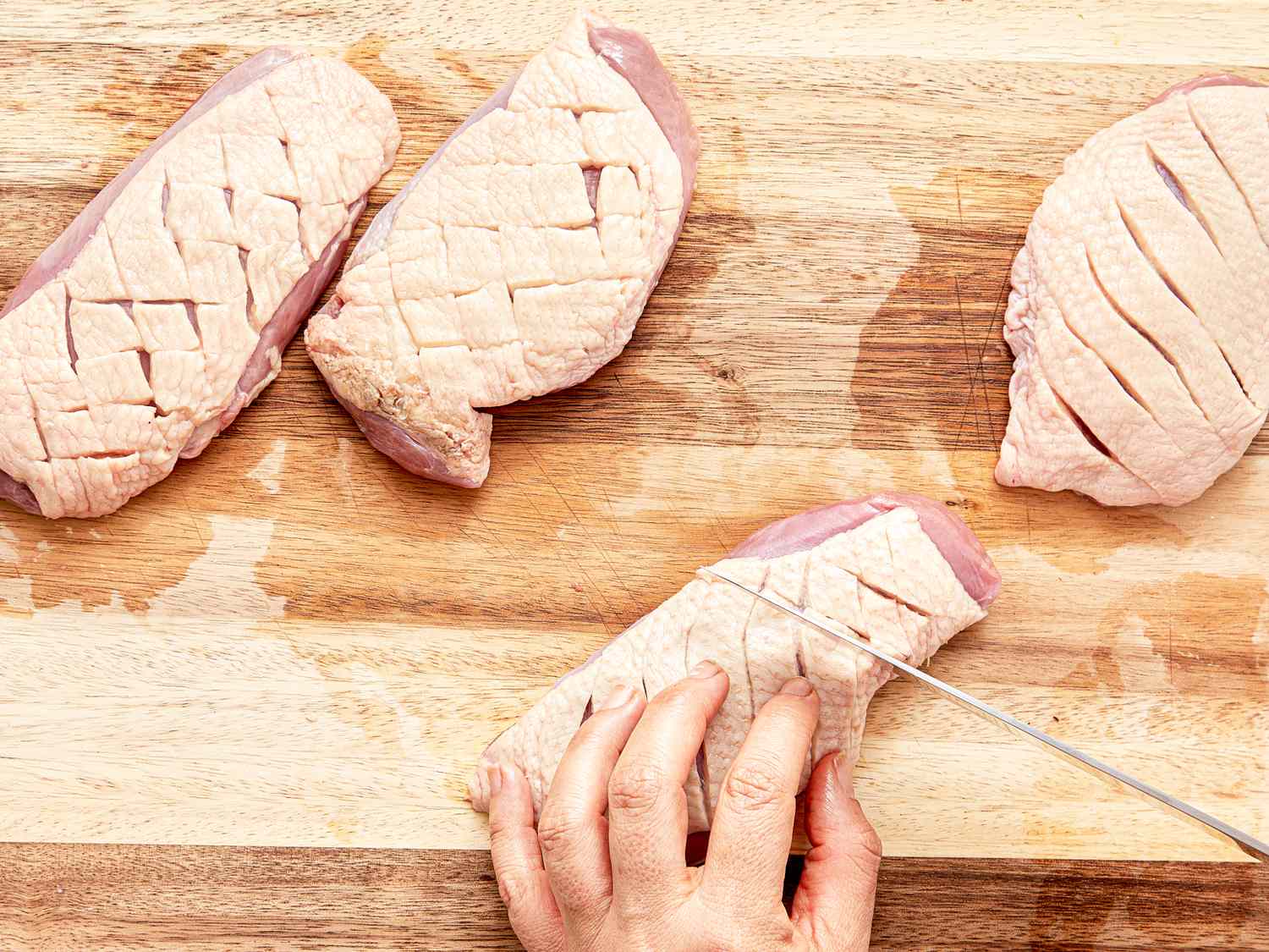 Slicing duck breasts with scored skin on a cutting board preparation step in cooking
