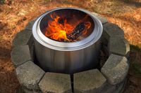 A metal fire pit burning logs, surrounded by a stone circle