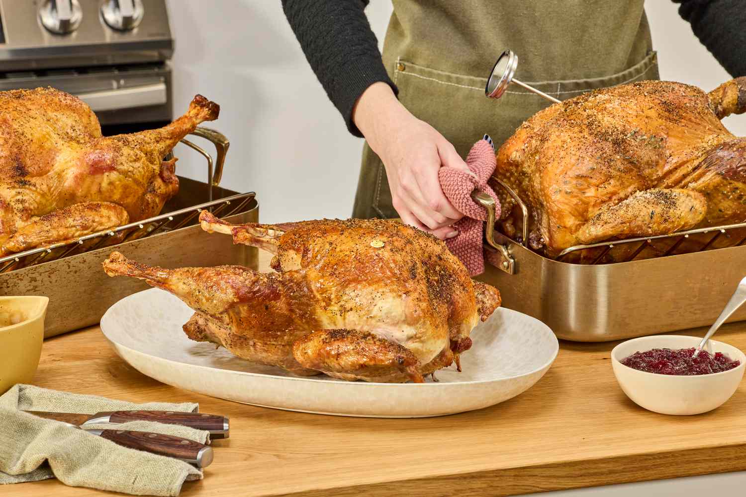 Three cooked turkeys on a kitchen countertop. A person is placing a turkey in a roasting pan onto the countertop.