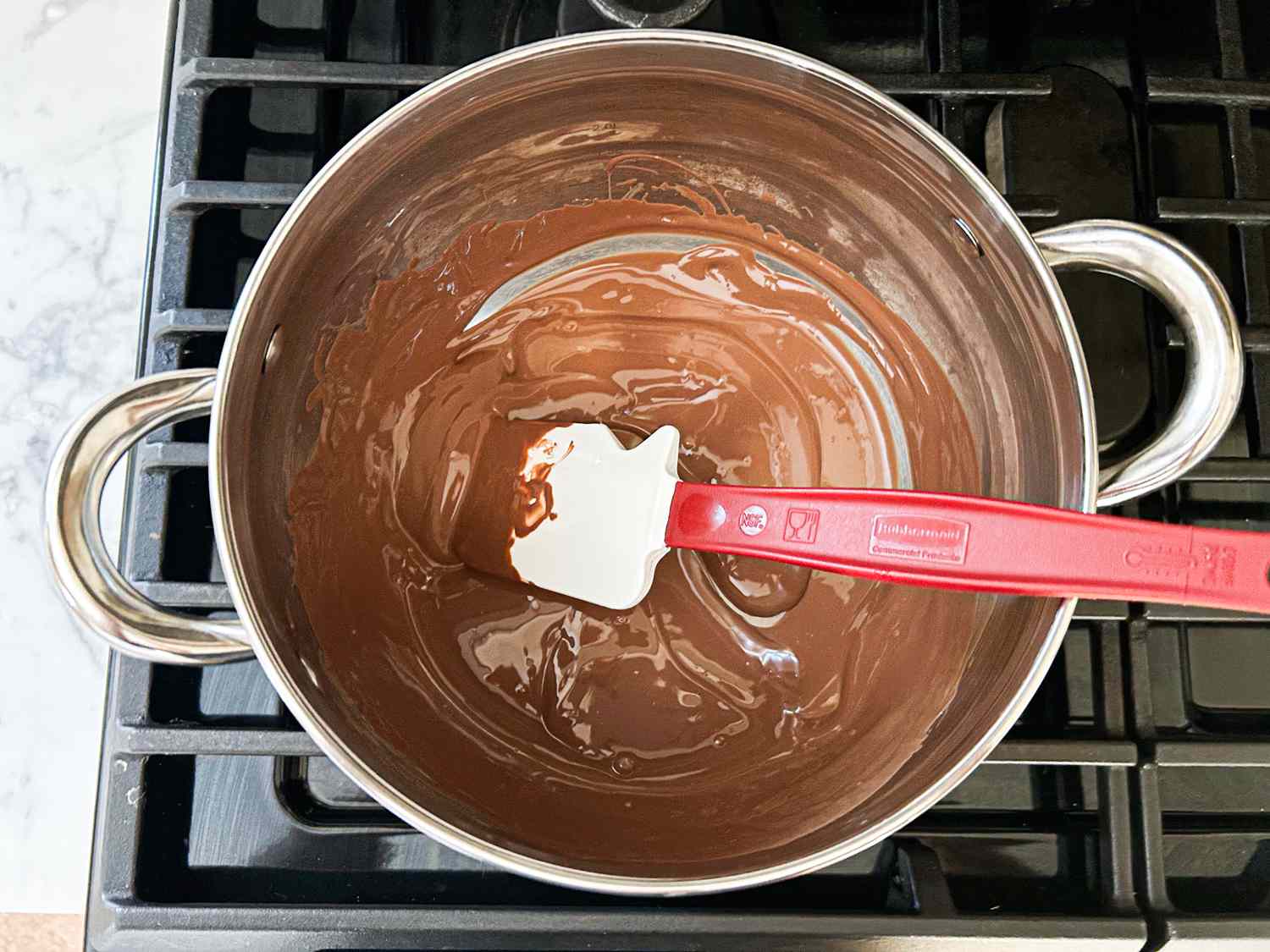 Chocolate melting in a pot on a stove with a spatula resting in the mixture