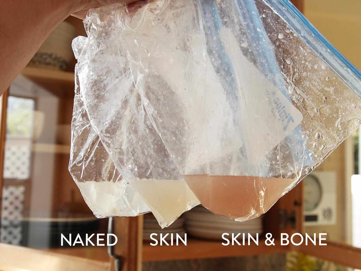 Three plastic bags holding juices collected from three sous vide cooked chicken breasts (one skinless and boneless with almost clear juices, one skin-on with pale juices, one skin-on and bone-in with dark pink juices).