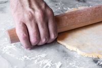A person rolling out dough with a J.K. Adams Maple French Rolling Pin on a floured surface