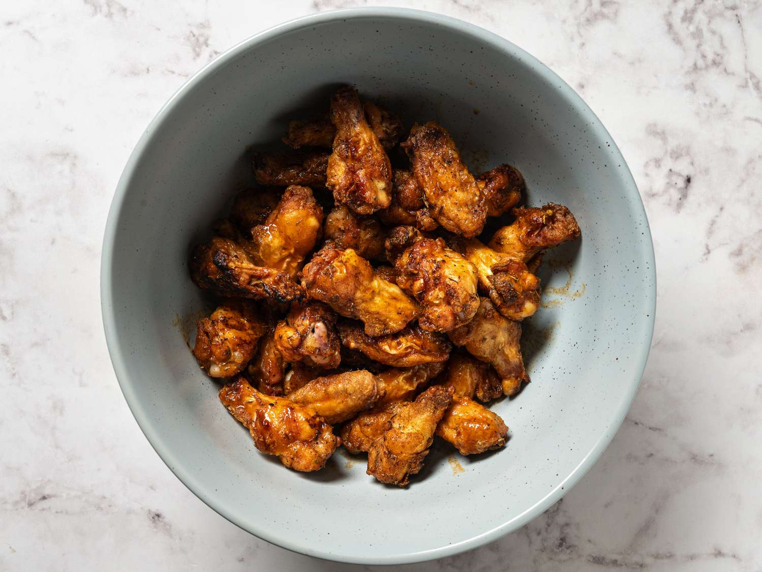 The cooked chicken wings coated with sauce inside of a large ceramic bowl.