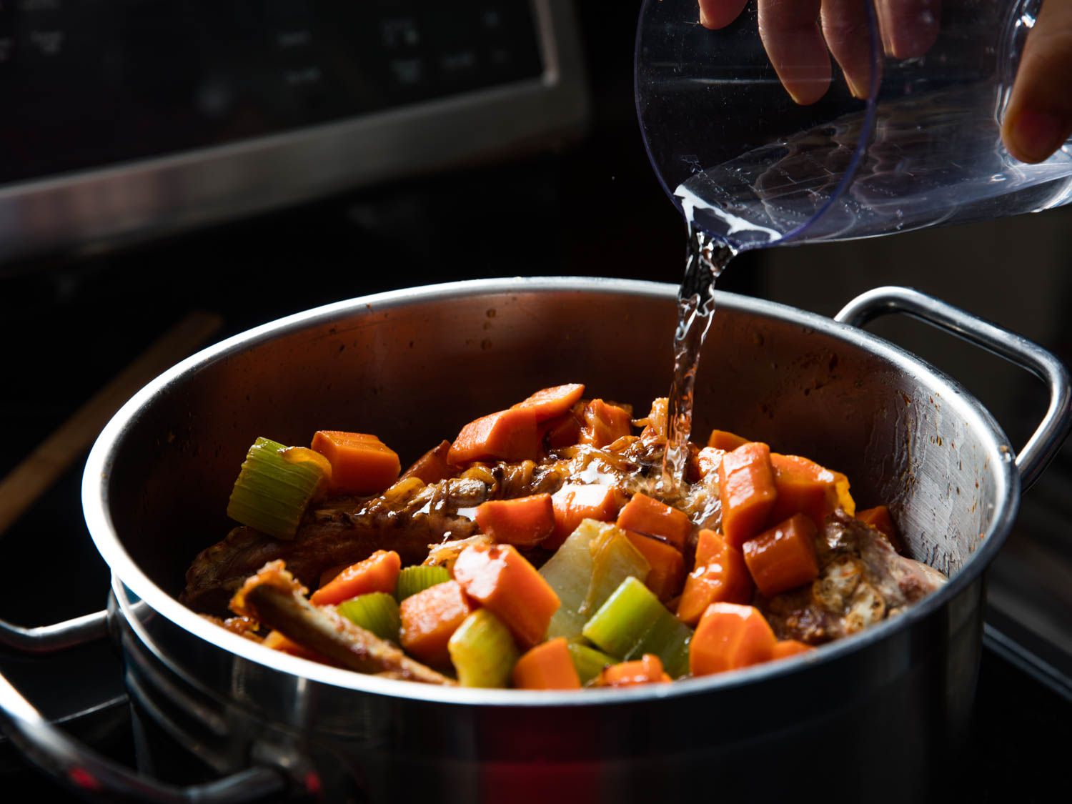 Adding water to stockpot full of browned vegetables and roasted turkey bone