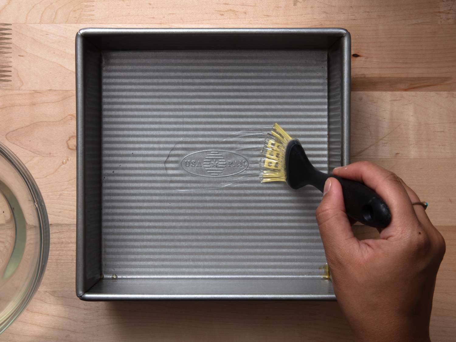 brushing an aluminum square pan with reserved coconut oil