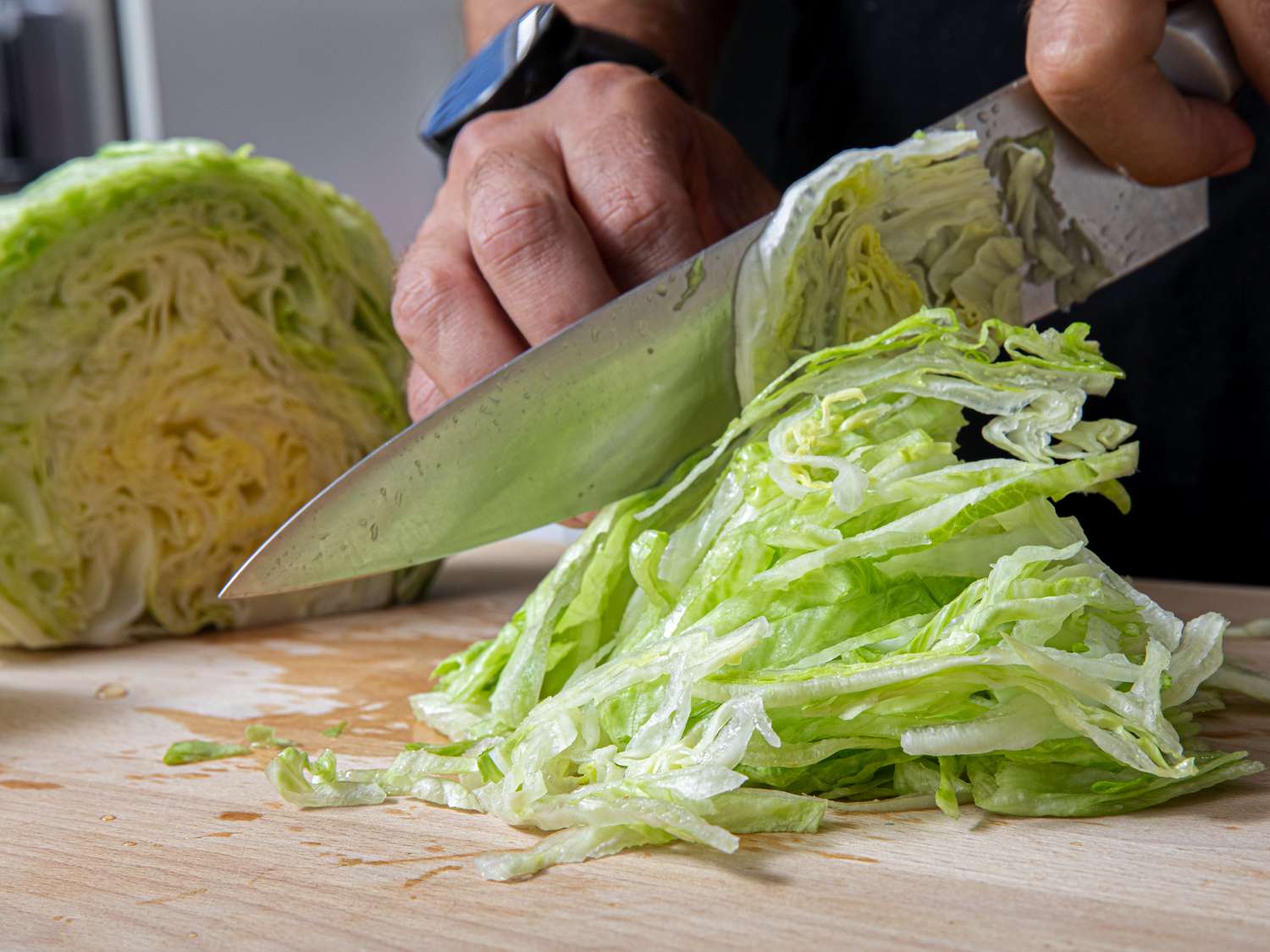 A hand cutting iceberg lettuce on a cutting board