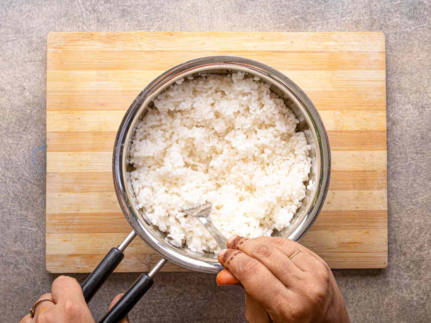 Hands holding a pot of cooked rice on a wooden board