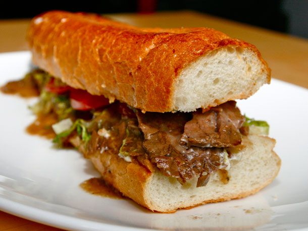 Closeup of a roast beef po'boy, served on a white plate.