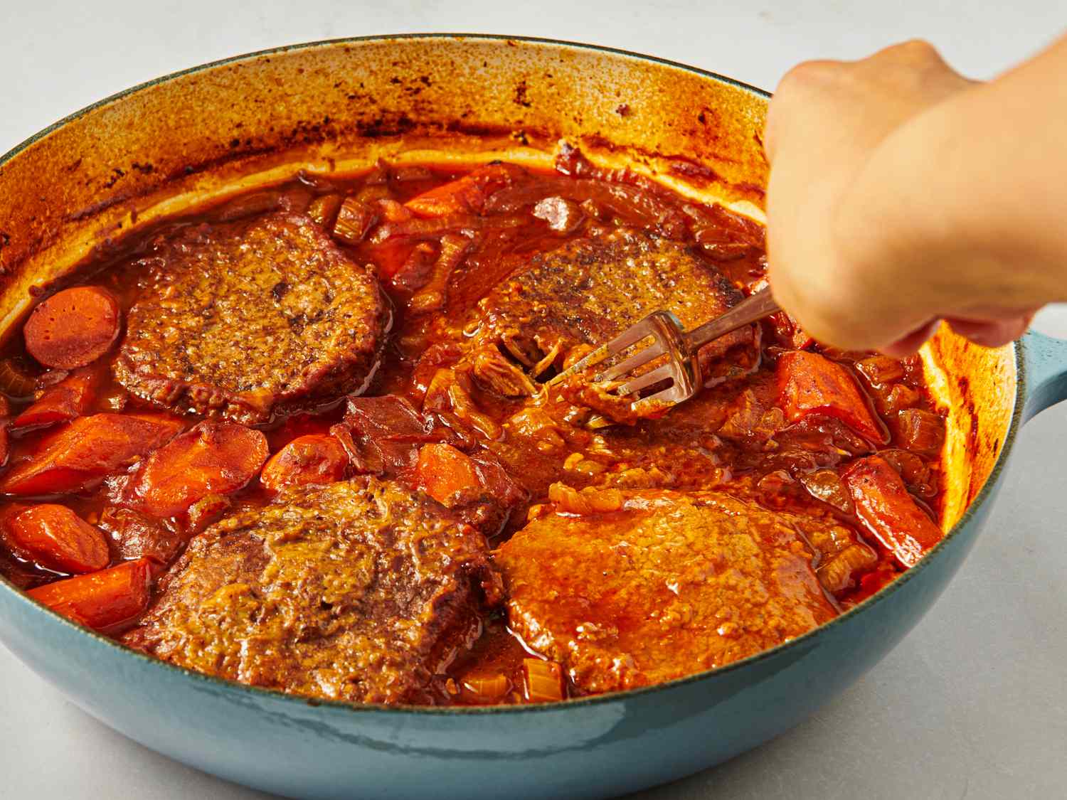 A person preparing Swiss steak in a skillet with a fork