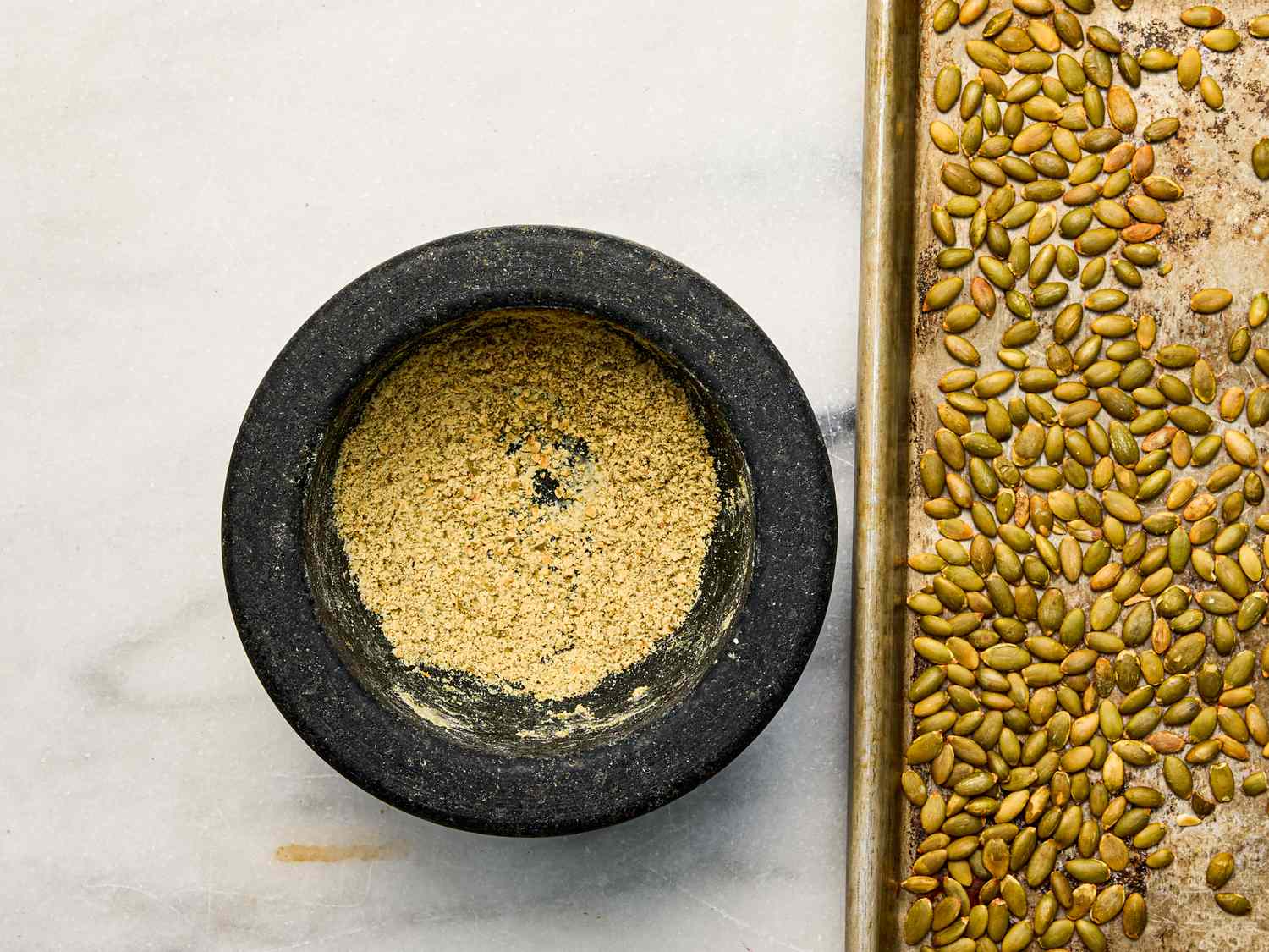 A mortar with ground mixture next to a tray of pepitas